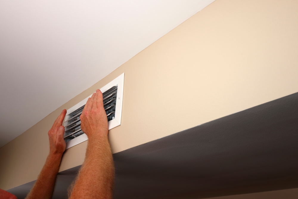 a man holding his hands up to an air vent to see how strong the airflow is