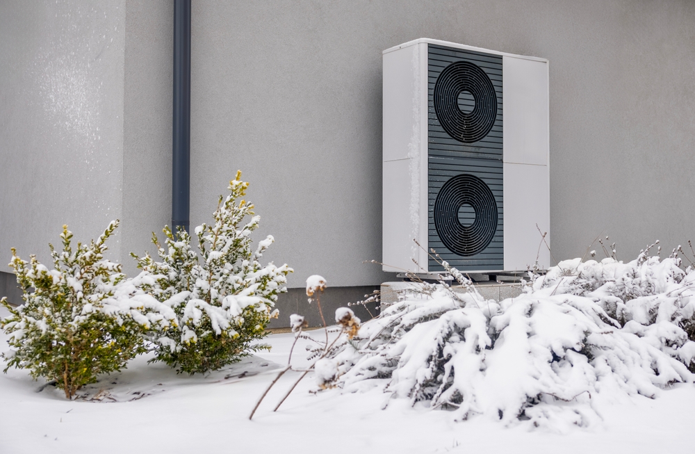 an outdoor heat pump unit surrounded by snowy grass and bushes