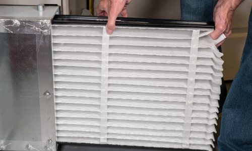 Senior man inserting a new air filter in a HVAC Furnace Senior caucasian man changing a folded air filter in the HVAC furnace system in basement of home