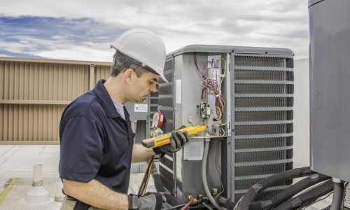 Hvac Tech working on a condensing unit Trained hvac technician holding a voltage meter, performing preventative maintenance on a air conditioning condenser unit.
